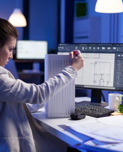 Woman architect analysing and matching blueprints for new building project Woman architect analysing and matching blueprints for new building project sitting at desk. Graphic designer using arhitecture prototype plans working overtime in corporate office late at night